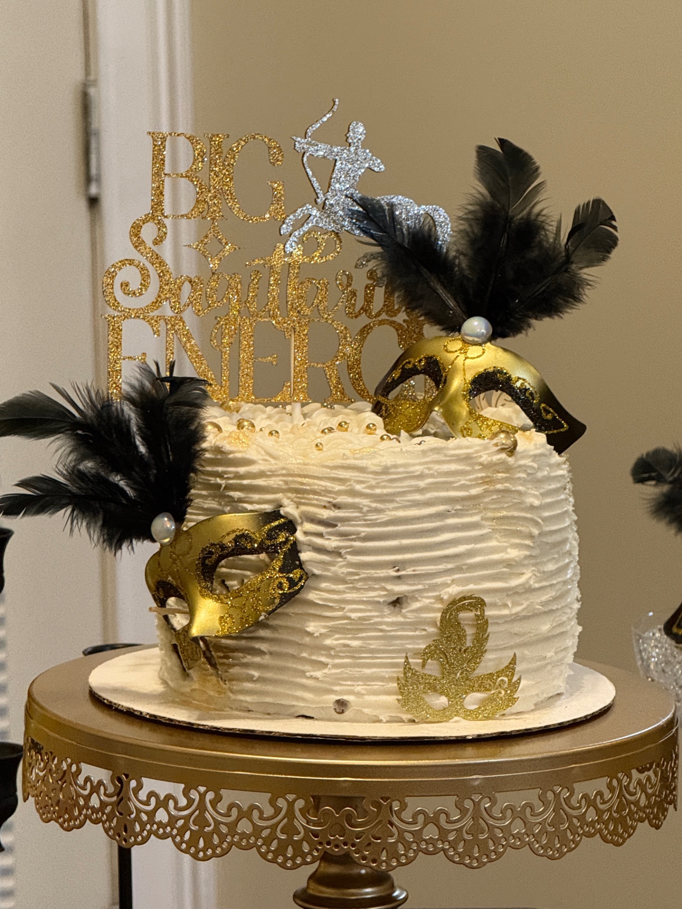 Sagittarius-themed white cake with gold masks and black feathers