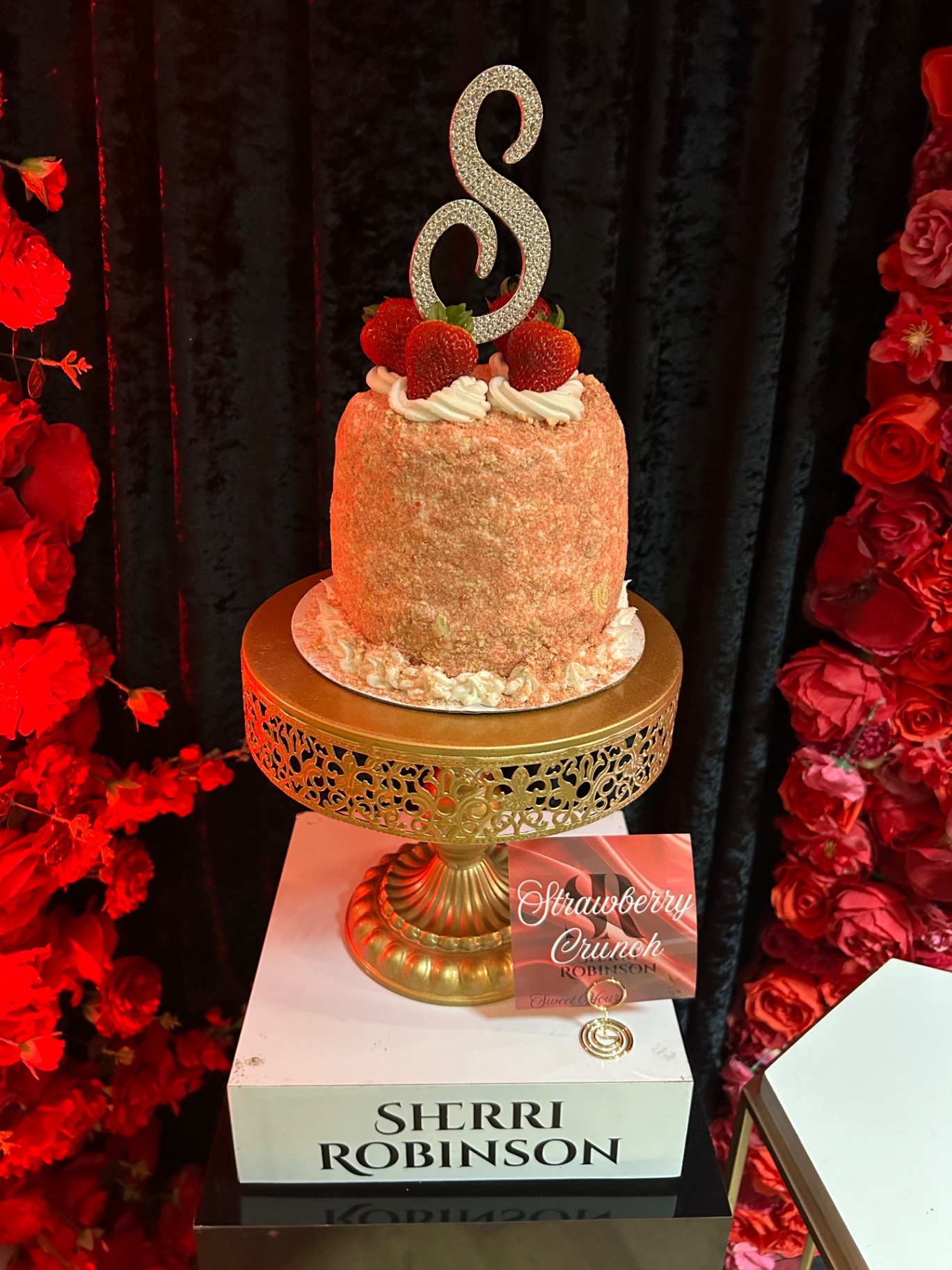 Strawberry crunch cake with monogram topper on gold pedestal