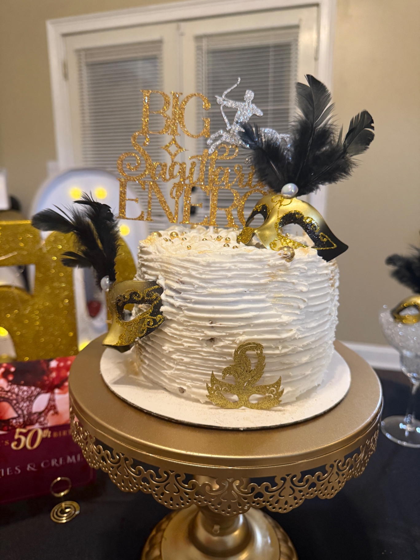 White masquerade cake with gold masks and feather accents