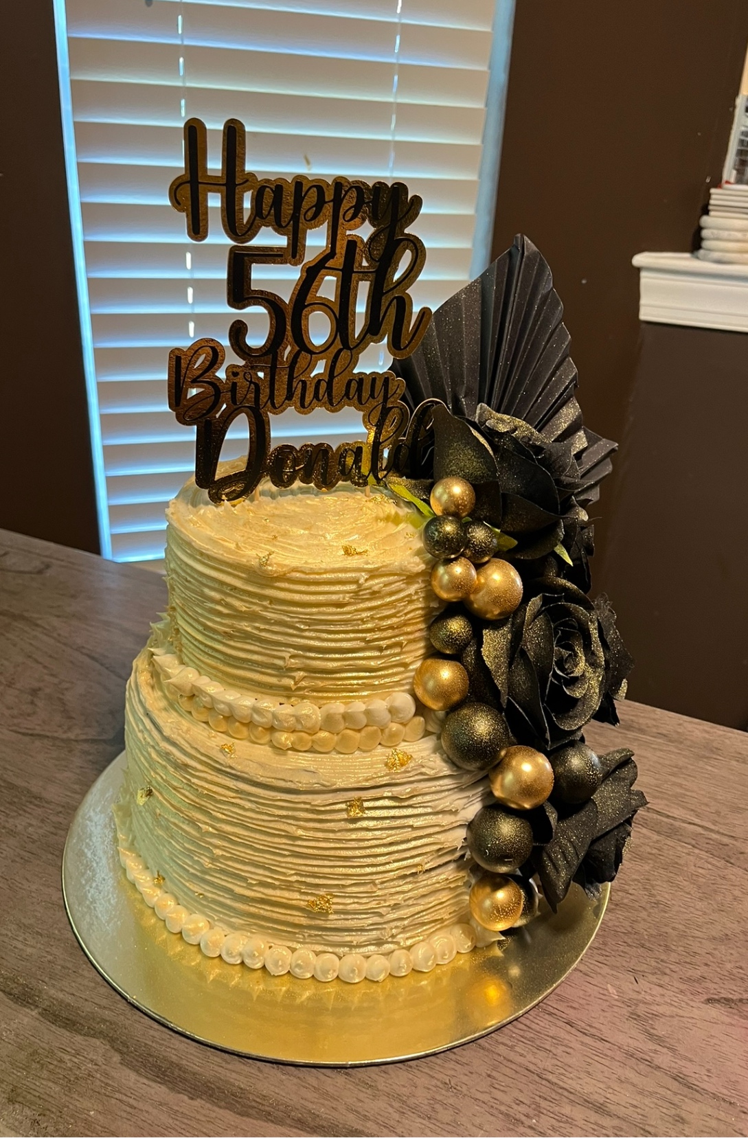 Two-tier gold cake with black roses and gilded accents
